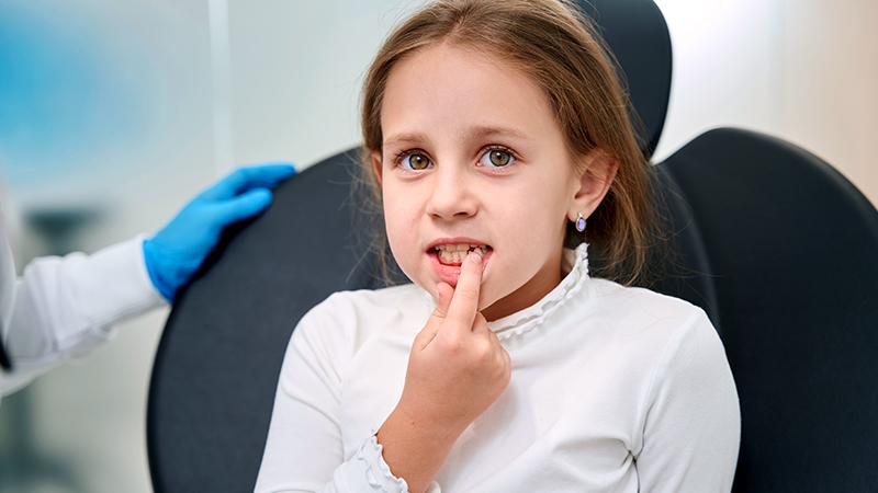 Teenage female sitting in dental chair, doctor with jaw model and toothbrush