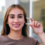 A smiling teenager holding an invisible teeth aligner.