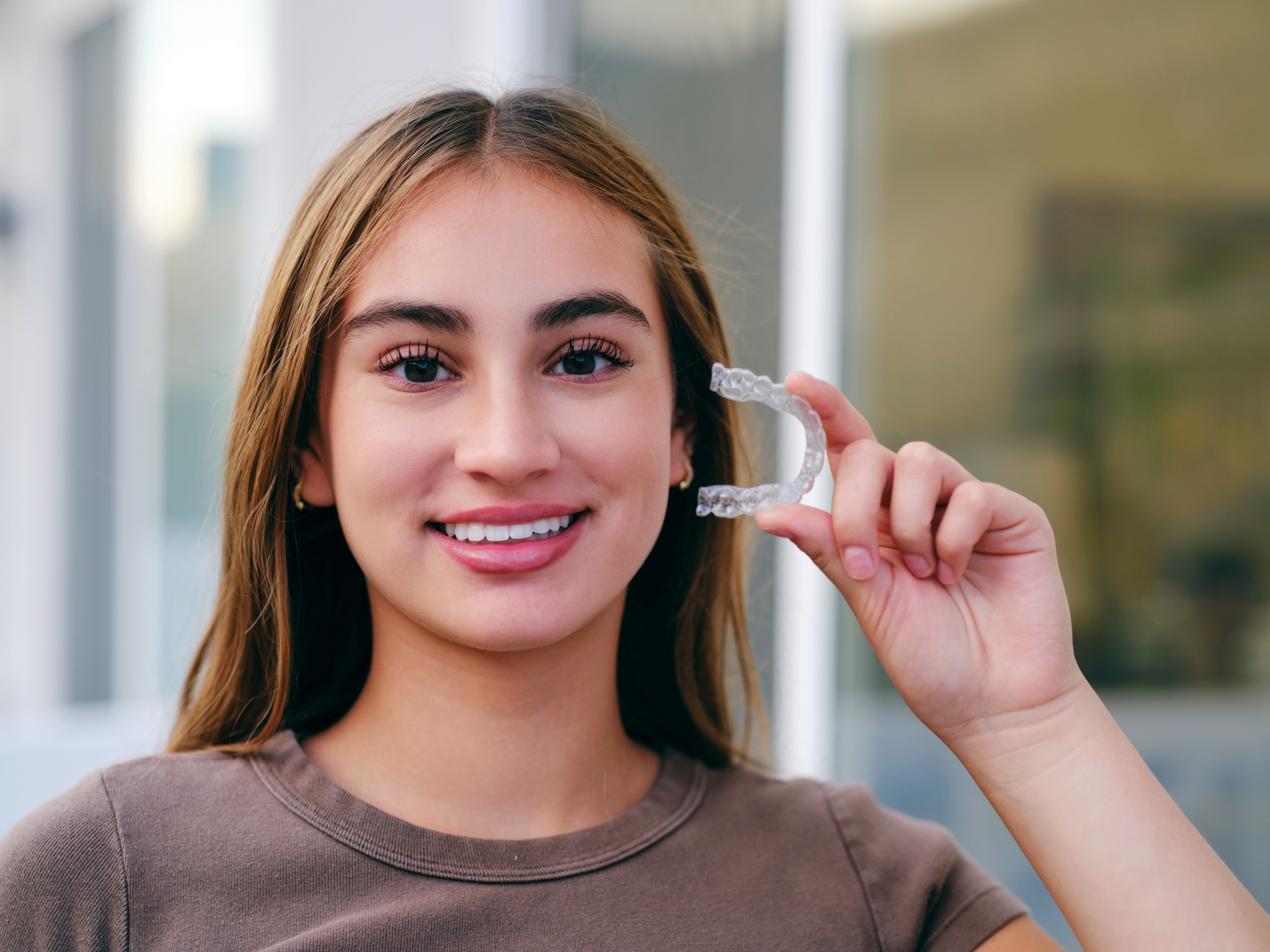 A smiling teenager holding an invisible teeth aligner.